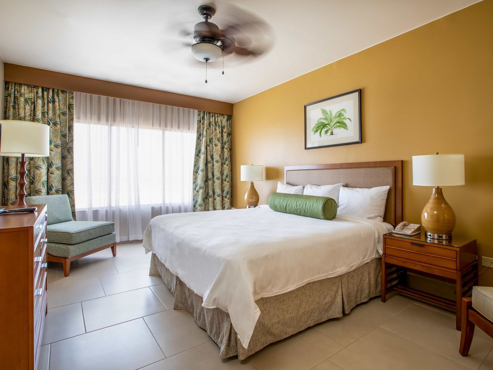A hotel room with a king size bed and a ceiling fan.