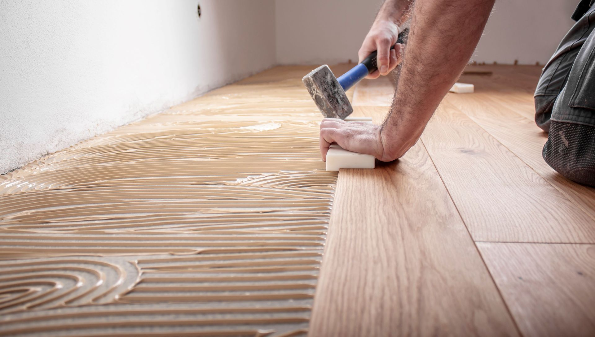 A man is laying a wooden floor with a hammer.