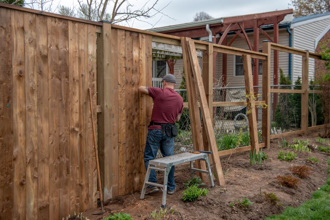 A man is working on a wooden fence in a backyard.