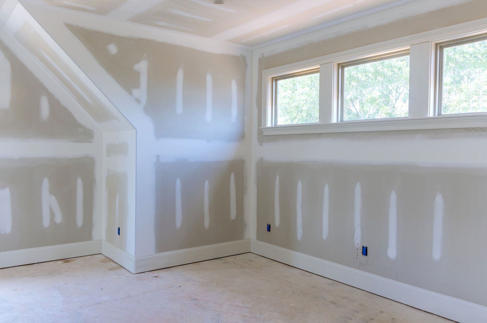 An empty room with drywall on the walls and two windows.