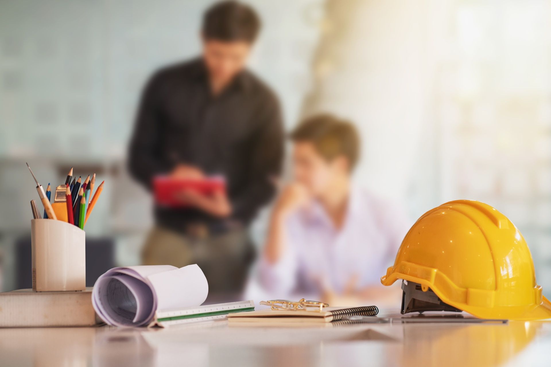 A hard hat , blueprints , pencils , and a clipboard are on a table.