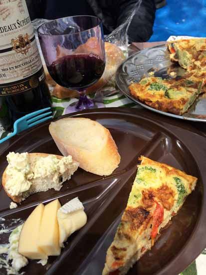 Picnic table with food: wine, bread, cheese, frittata.