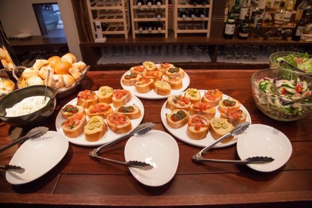 Buffet spread with bruschetta, bread rolls, salad, and appetizers on a wooden surface.