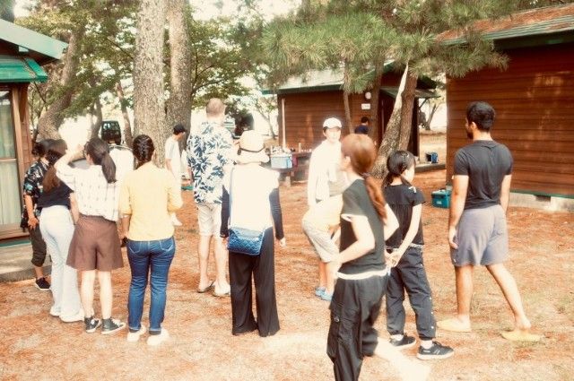 Group of people standing outside wooden cabins under trees.