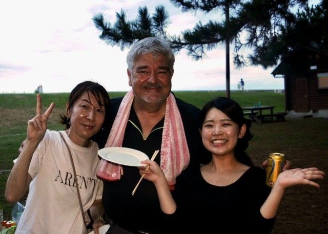 Three people smiling at an outdoor gathering. One makes a peace sign, another holds a plate.