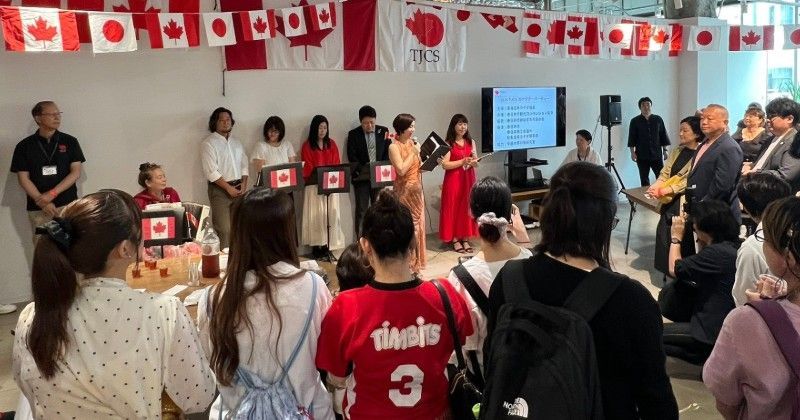 Audience watching a group presentation with Canadian flag decorations and a speaker at the front.