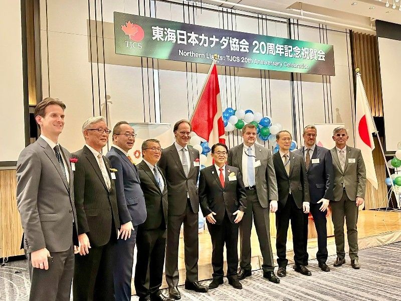 Group of men posing at an event with Canadian and Japanese flags in background.