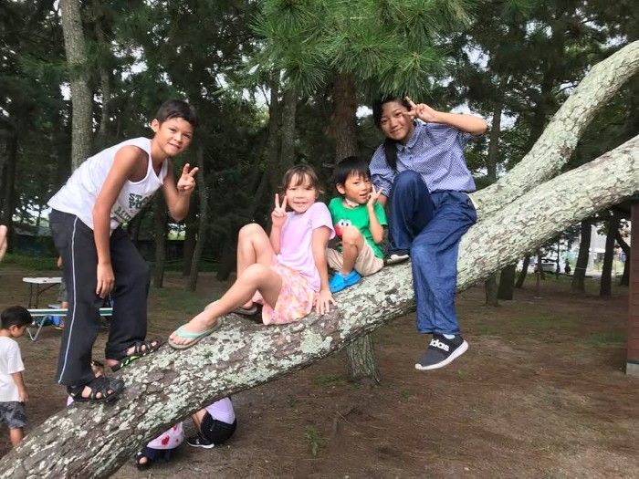 Children posing on a large tree branch in a park, with two adults nearby