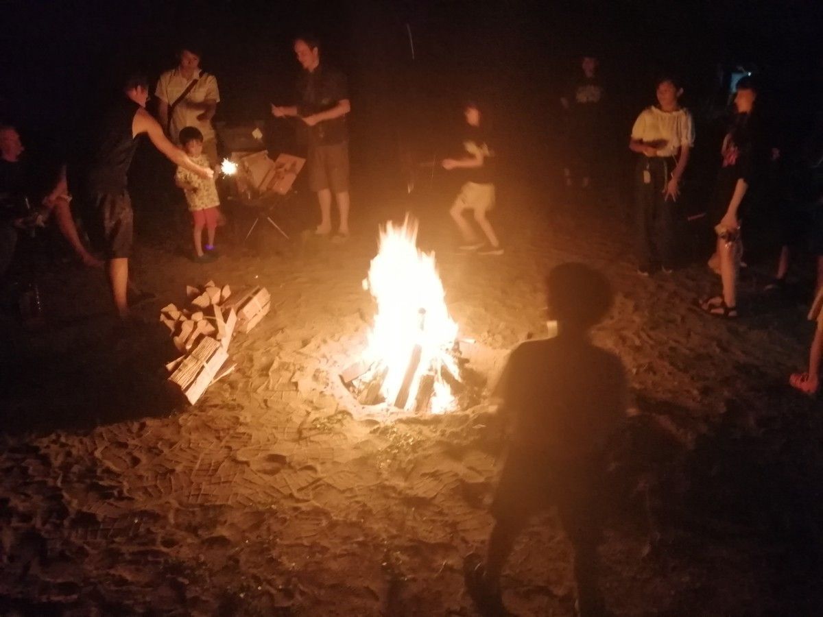 People gathered around a campfire at night in a dark outdoor clearing.