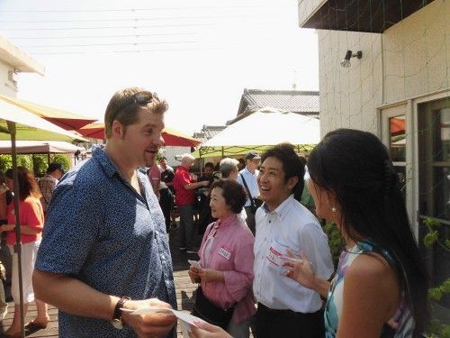 People conversing outdoors; man in blue shirt and two others, near a building; sunny day.