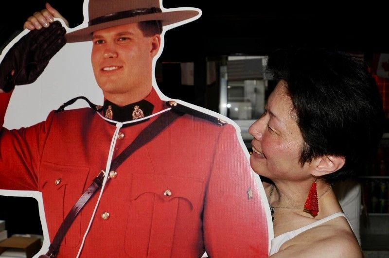 Woman smiles at cardboard cutout of a Mountie in a red uniform and hat.