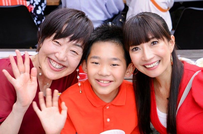 Three people smiling and waving; the middle person is wearing an orange shirt.