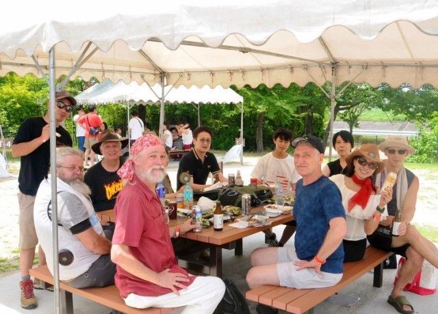 People at picnic table under a white tent; food and drinks on table.