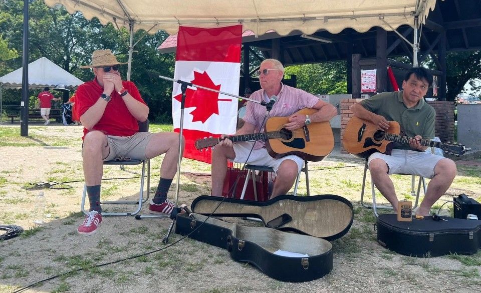 Three musicians playing guitars outdoors, with a Canadian flag in the background.