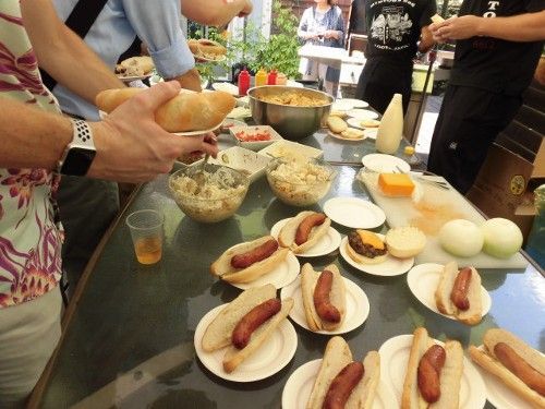 People at a picnic table with hot dogs, sides, and condiments.