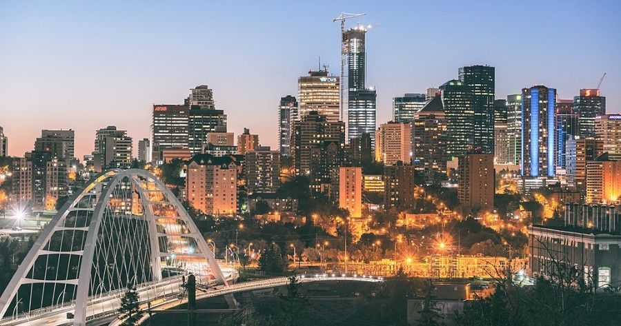 City skyline at dusk with lit bridge in foreground. Skyscrapers, buildings with lights, blue sky.