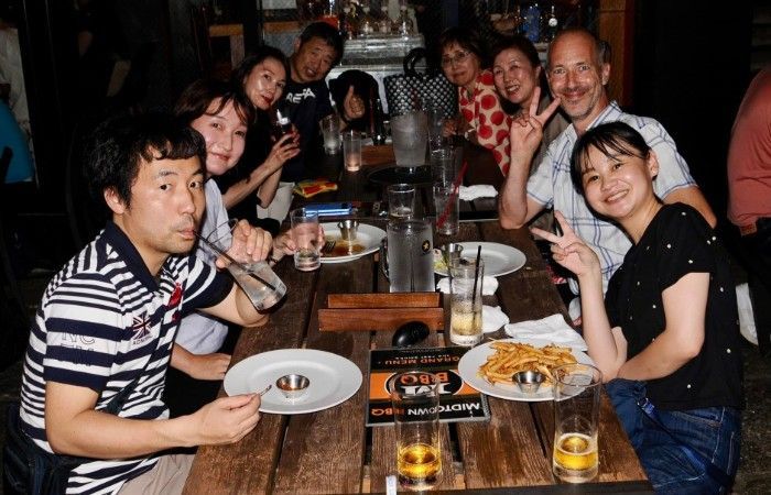 Group of people at a restaurant table; some are smiling, and one is giving a peace sign.