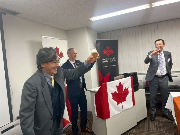 Three men toasting with drinks in a room with Canadian flags; celebratory atmosphere.