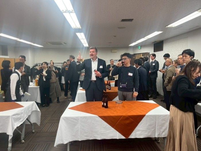 People at a gathering drinking and socializing in a room with tables and bright lighting.