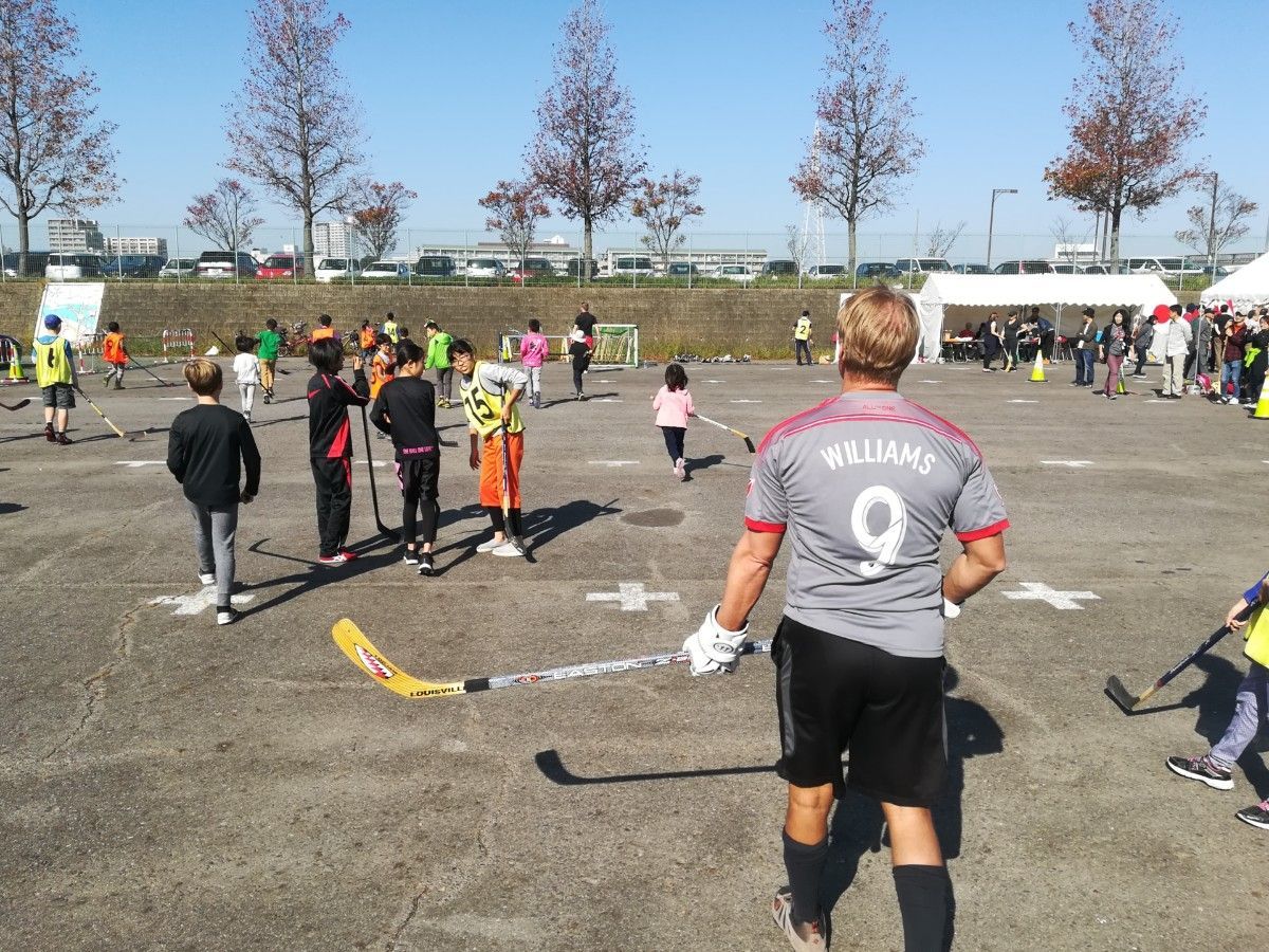 Youth hockey practice on an outdoor rink, players in jerseys and helmets gathered under bare trees.