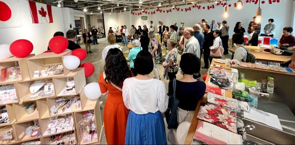 Crowd at an event in a room decorated with Canadian flags, shopping at display shelves.