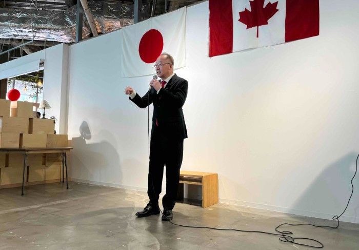 Kasugai Mayor speaking at event with Japanese and Canadian flags in background.
