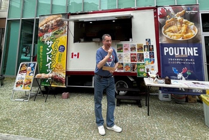 Man stands in front of a Canadian food truck selling sandwiches and poutine.