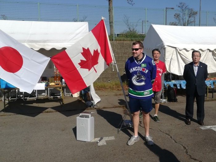 Man in Canucks jersey holding a Canadian flag with Japanese flag and men in front of tents.
