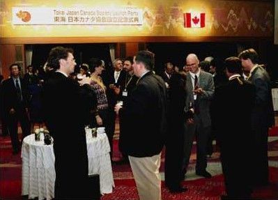 People at a Japan-Canada event; Canadian flag and table with drinks in background.