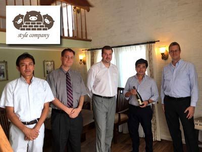 Five people stand inside a building, one holding a wine bottle. A 