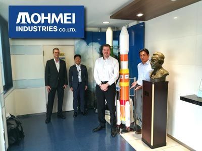 Four men stand near rocket models, a bust, and the 