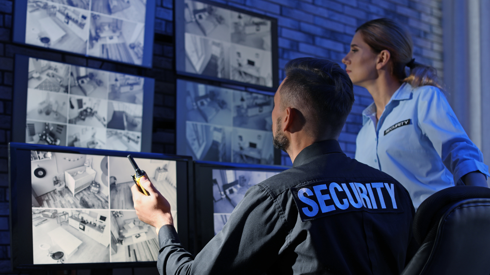 a man and a woman are looking at monitors in a security room .