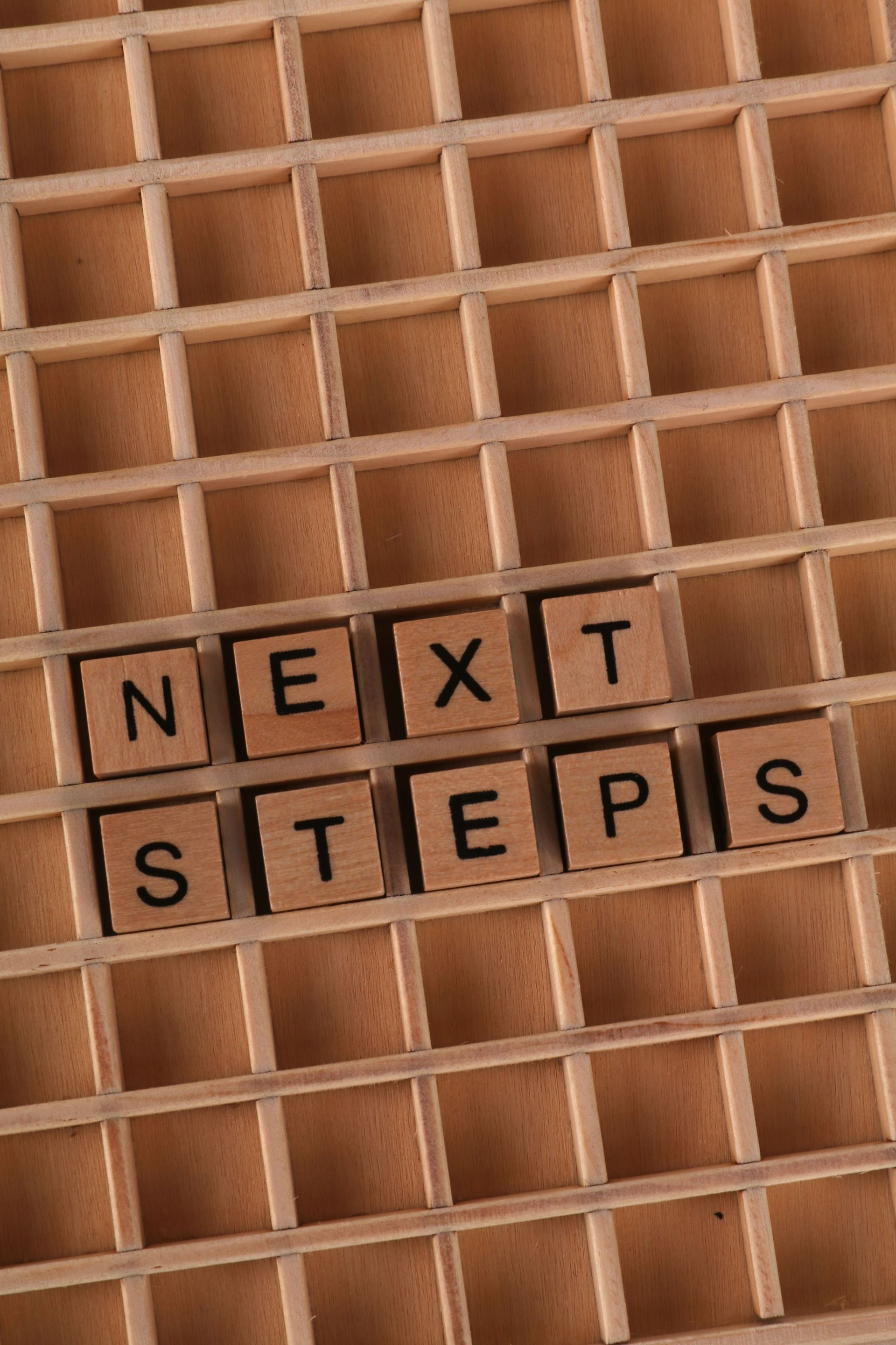 Scrabble tiles spelling “NEXT STEPS” on a wooden grid background