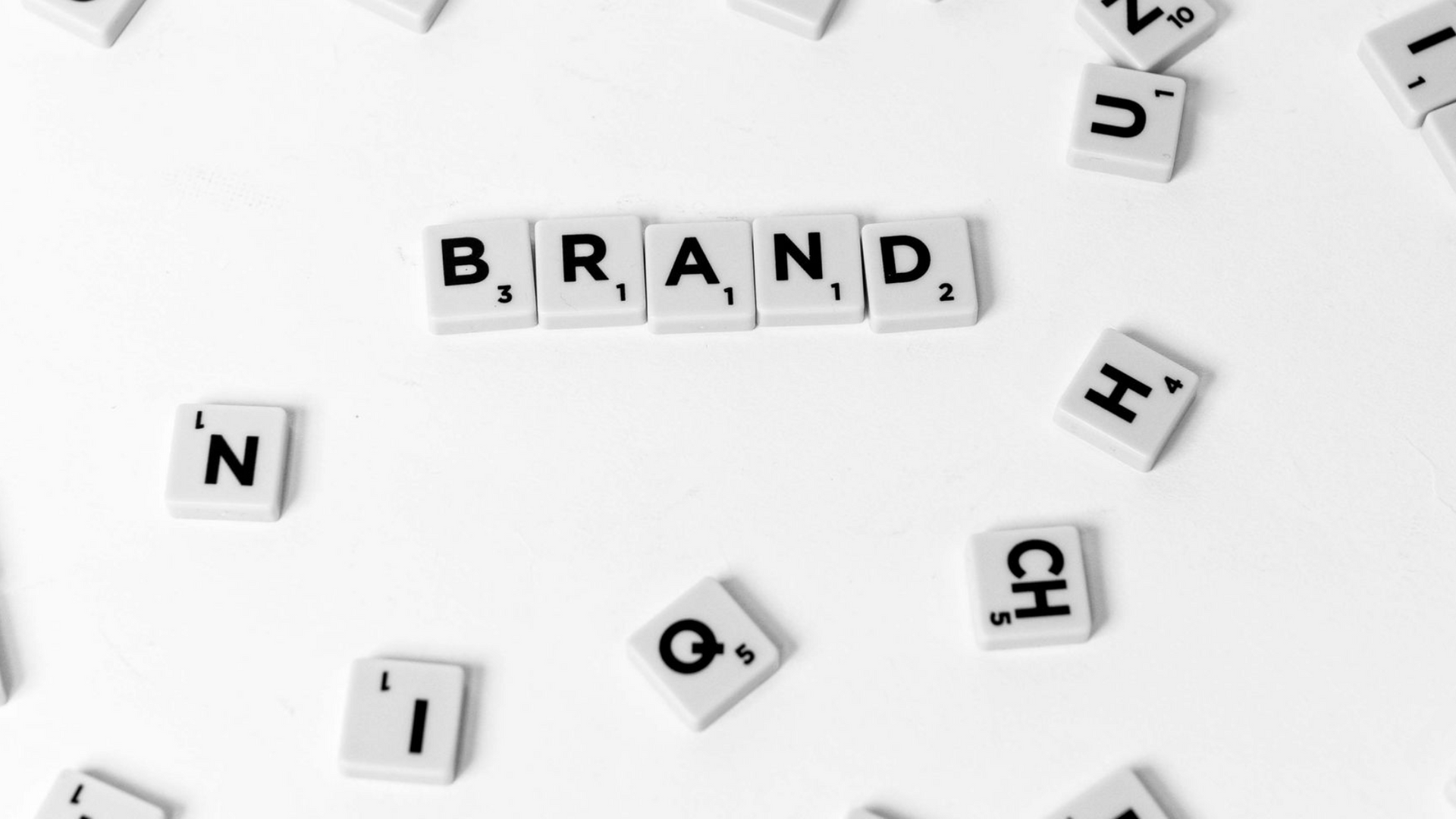 Scrabble tiles spelling “BRAND” on a light background, with scattered letter tiles around them