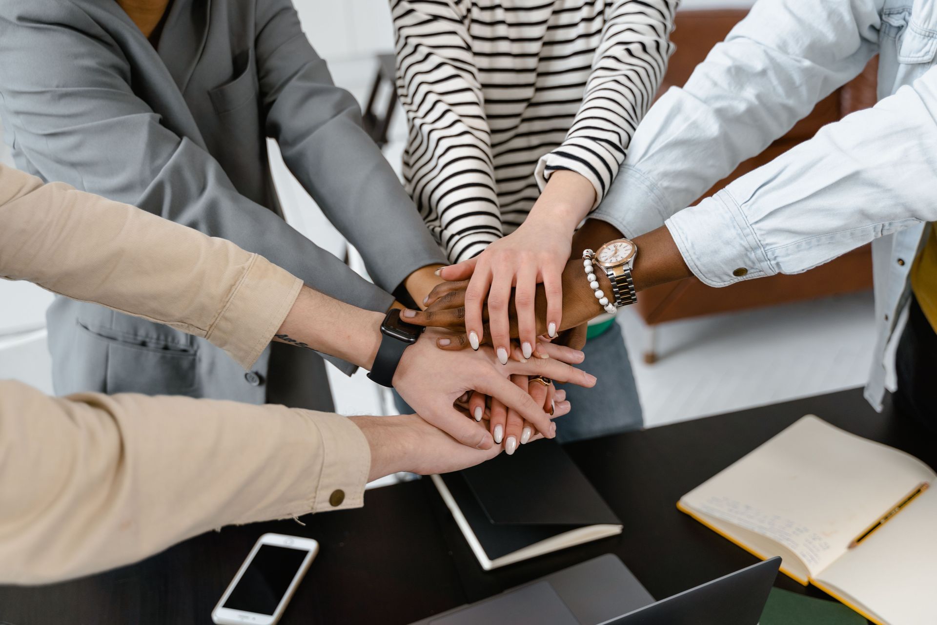 Hands stacked together over a table with notebooks and a smartphone, showing team collaboration.