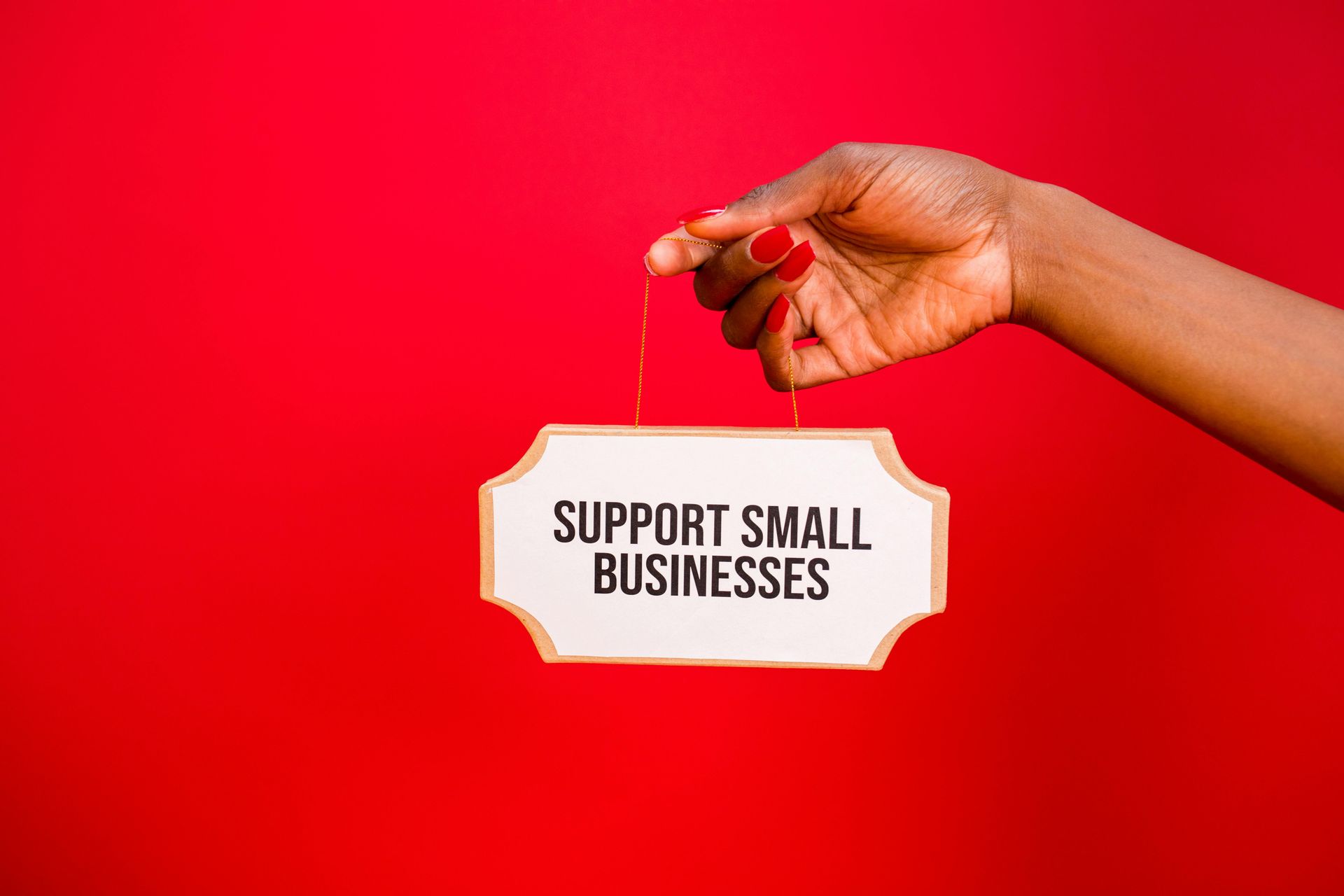 Hand holding a small sign reading “Support Small Businesses” against a bright red background