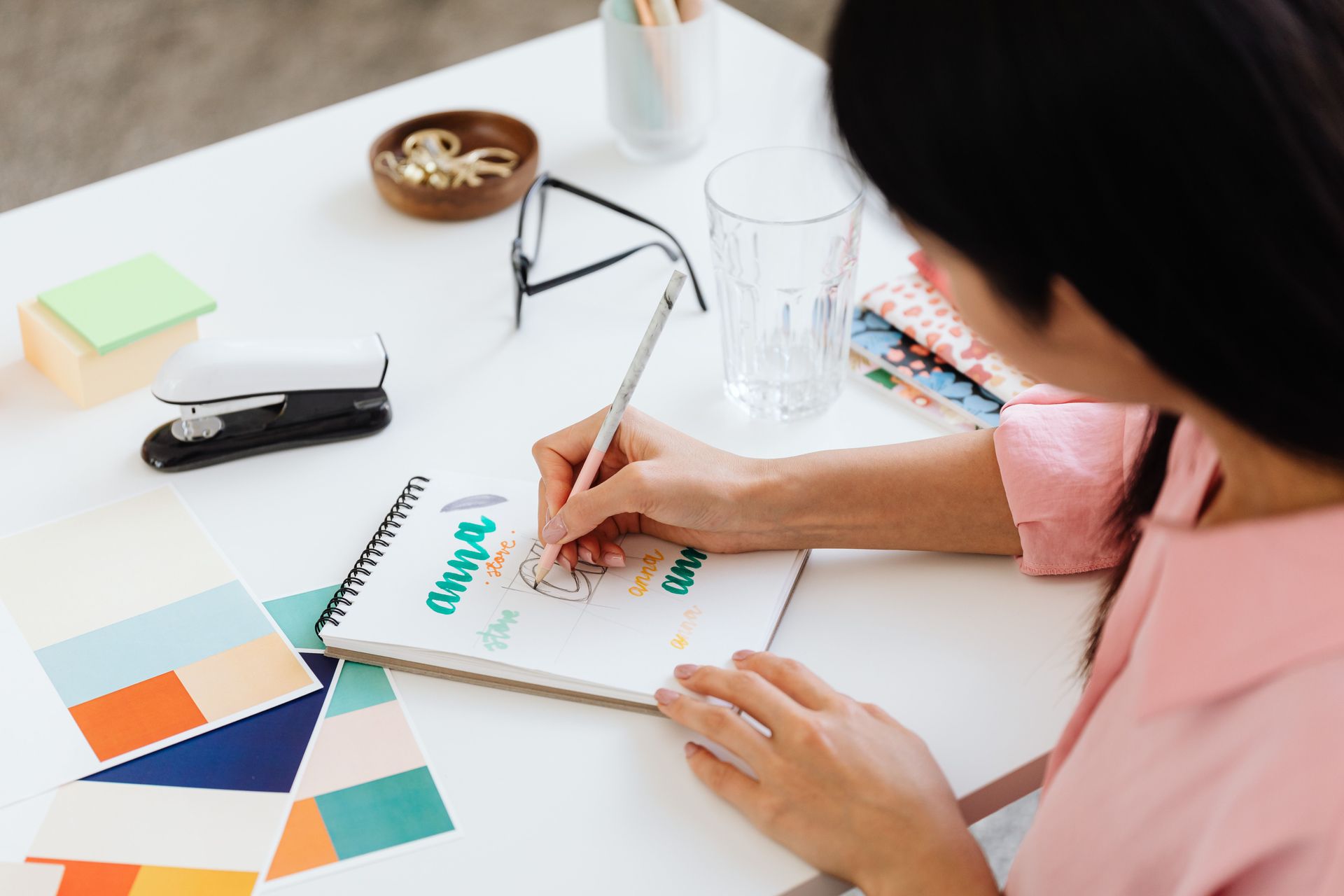 Person sketching at a desk with color swatches, glasses, and design tools