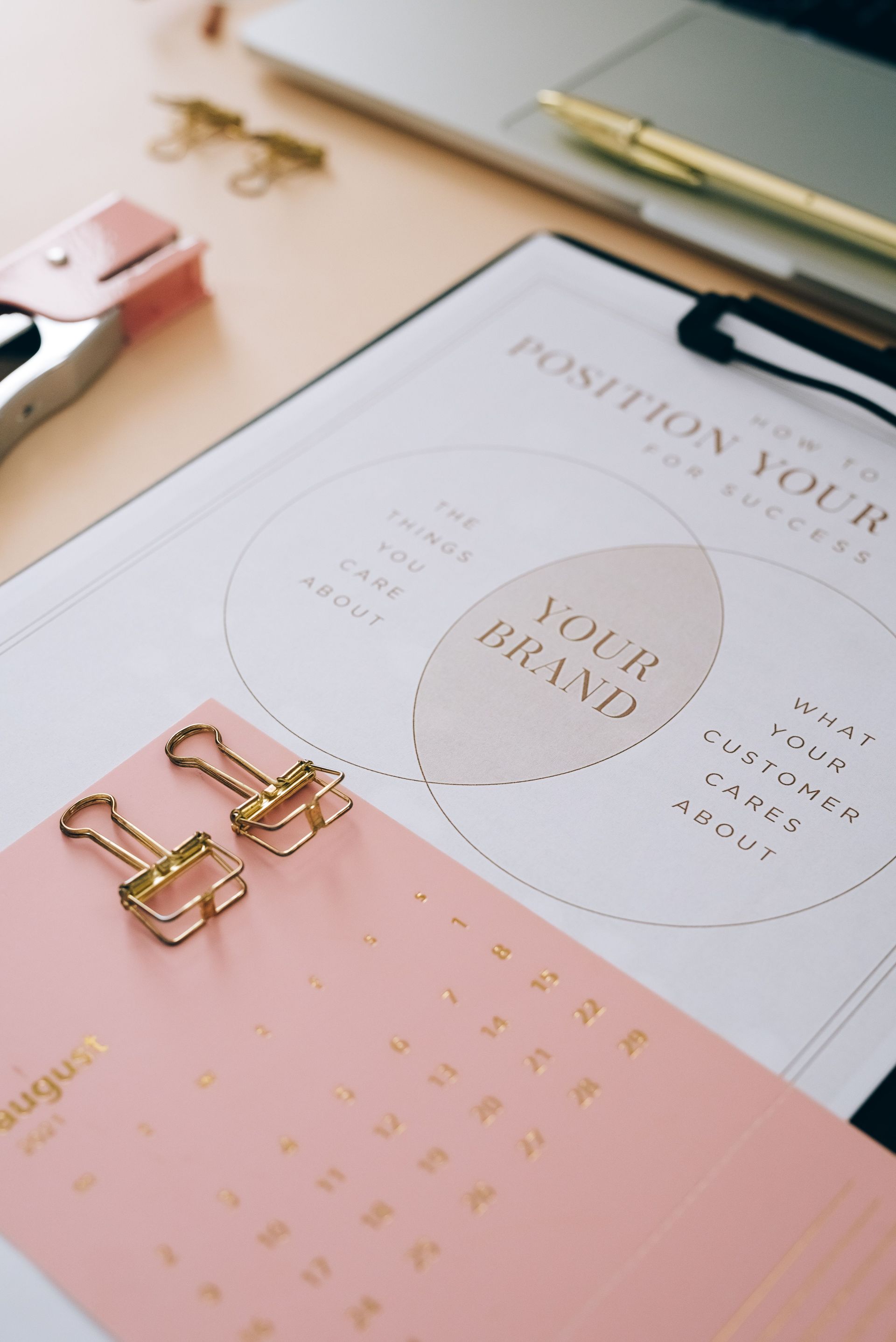 Pastel stationery with a planner, gold paper clips, and a pink calendar page on a desk