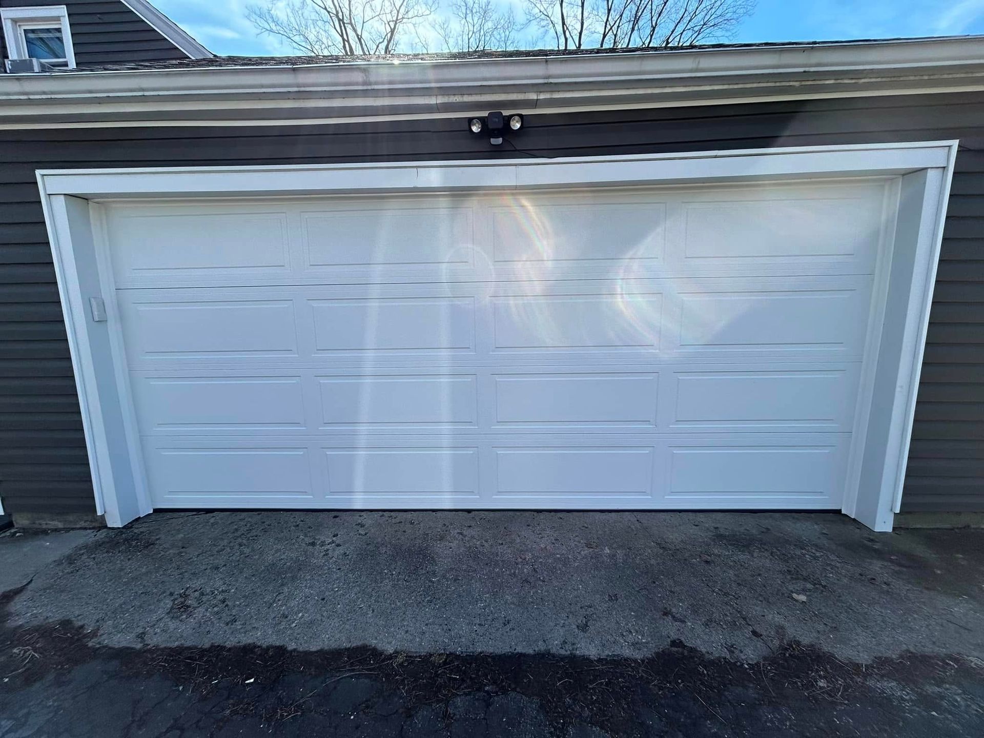 A white, rectangular garage door with horizontal panels, set in a dark-sided building with a concrete driveway.