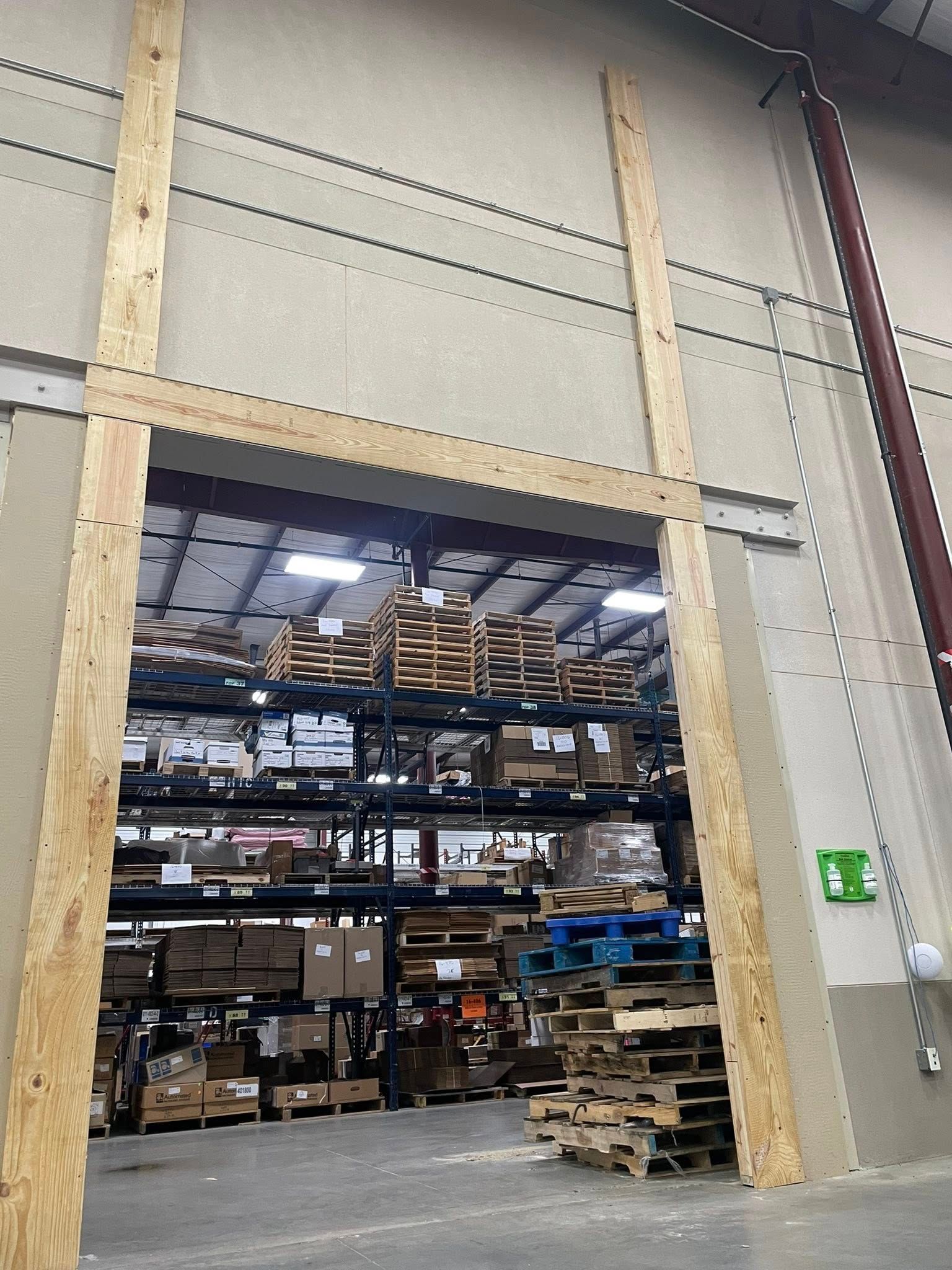 A view through an industrial doorway framed with wood into a warehouse filled with pallet racks and stacked materials.