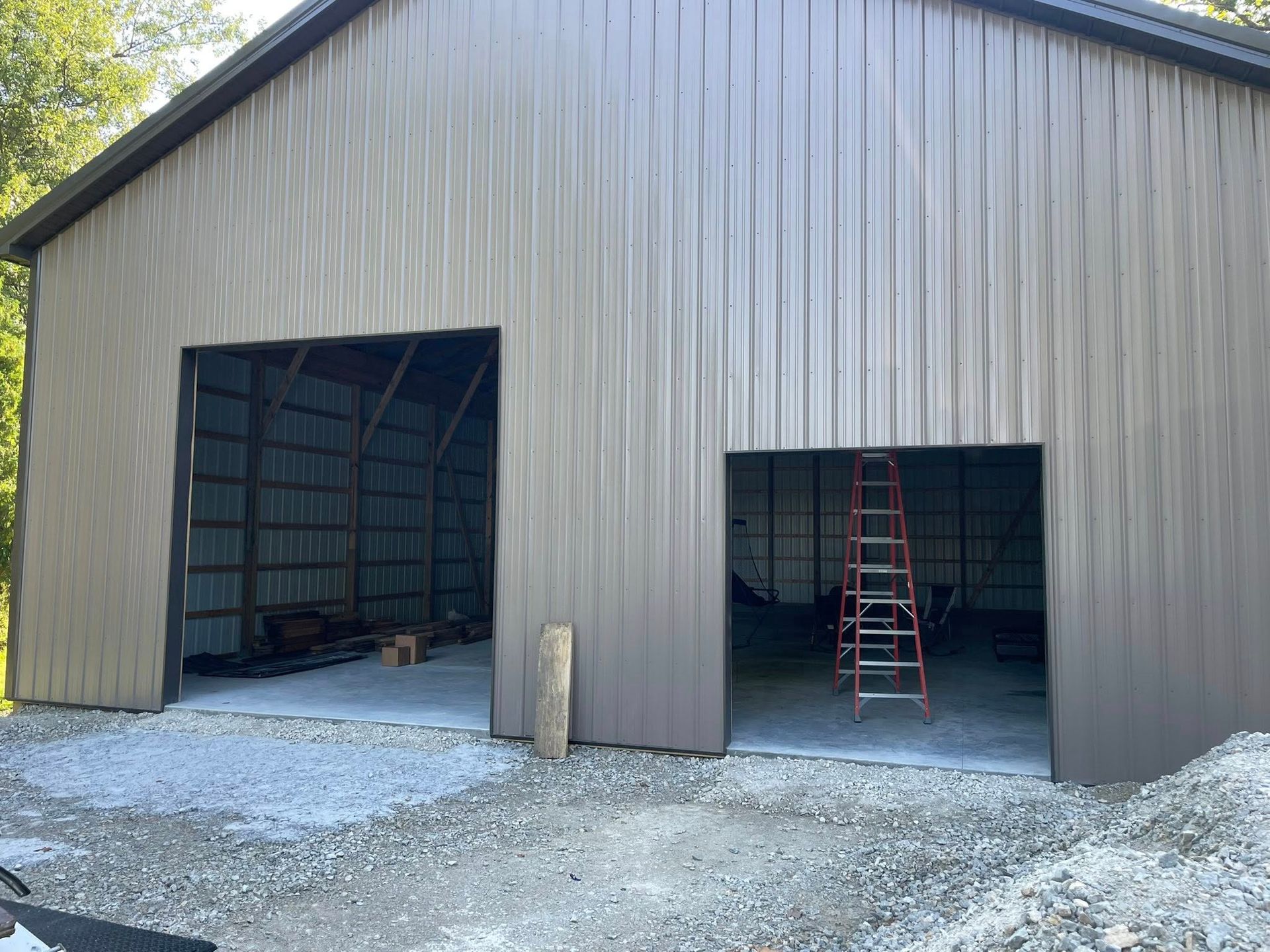 A tan metal pole barn with two open garage-style bays and a red ladder visible inside one of the openings.