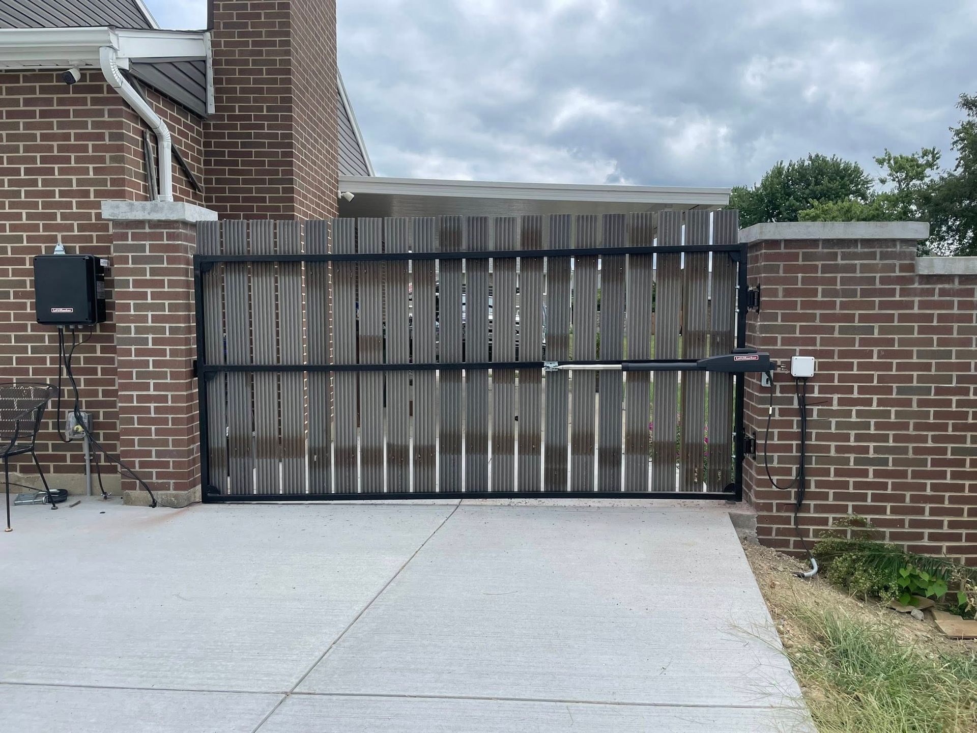 A wooden driveway gate with a metal frame and electric motor opener between brick pillars on a concrete driveway.