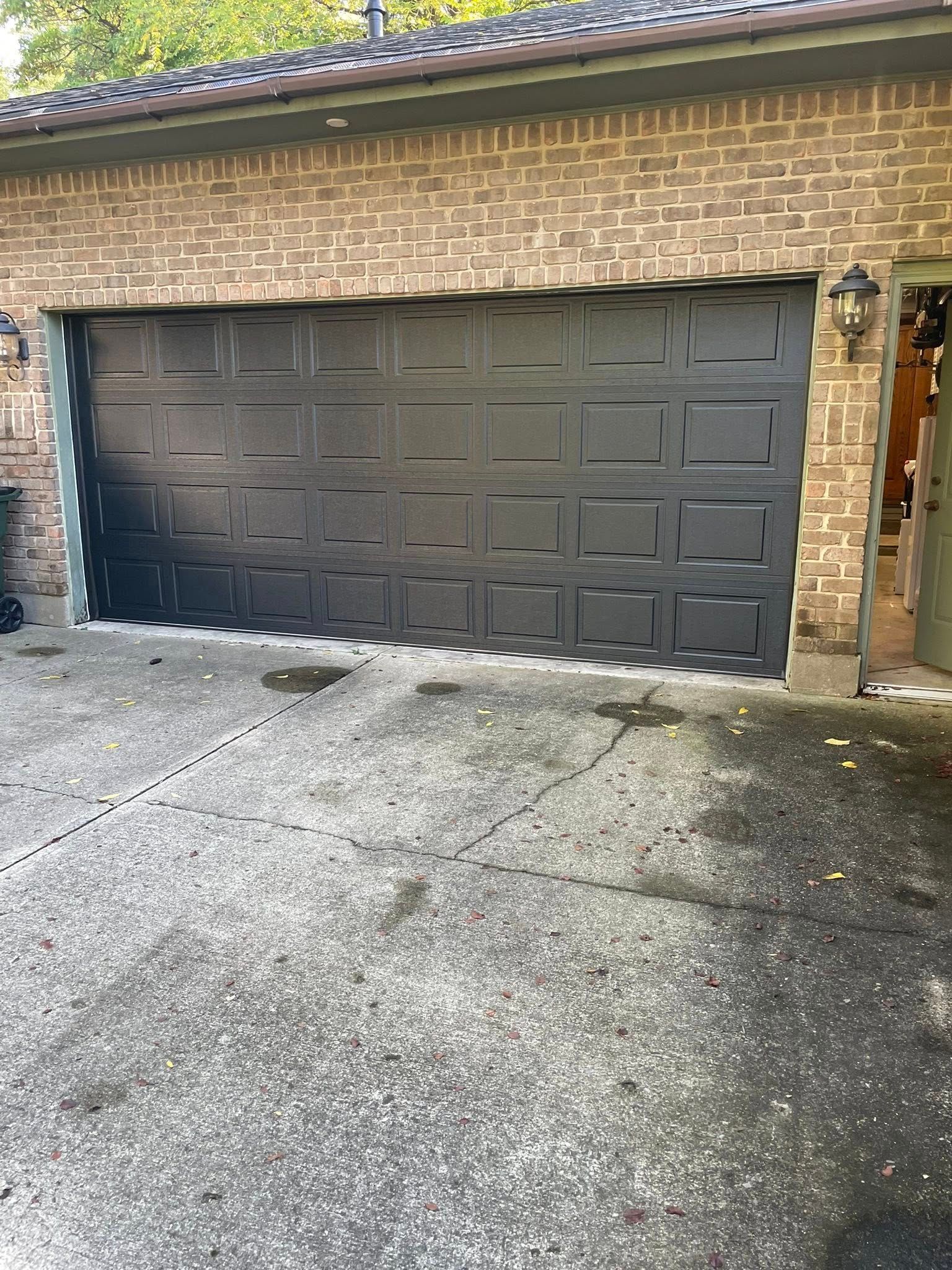 A black multi-panel garage door installed in a brick house with a concrete driveway.