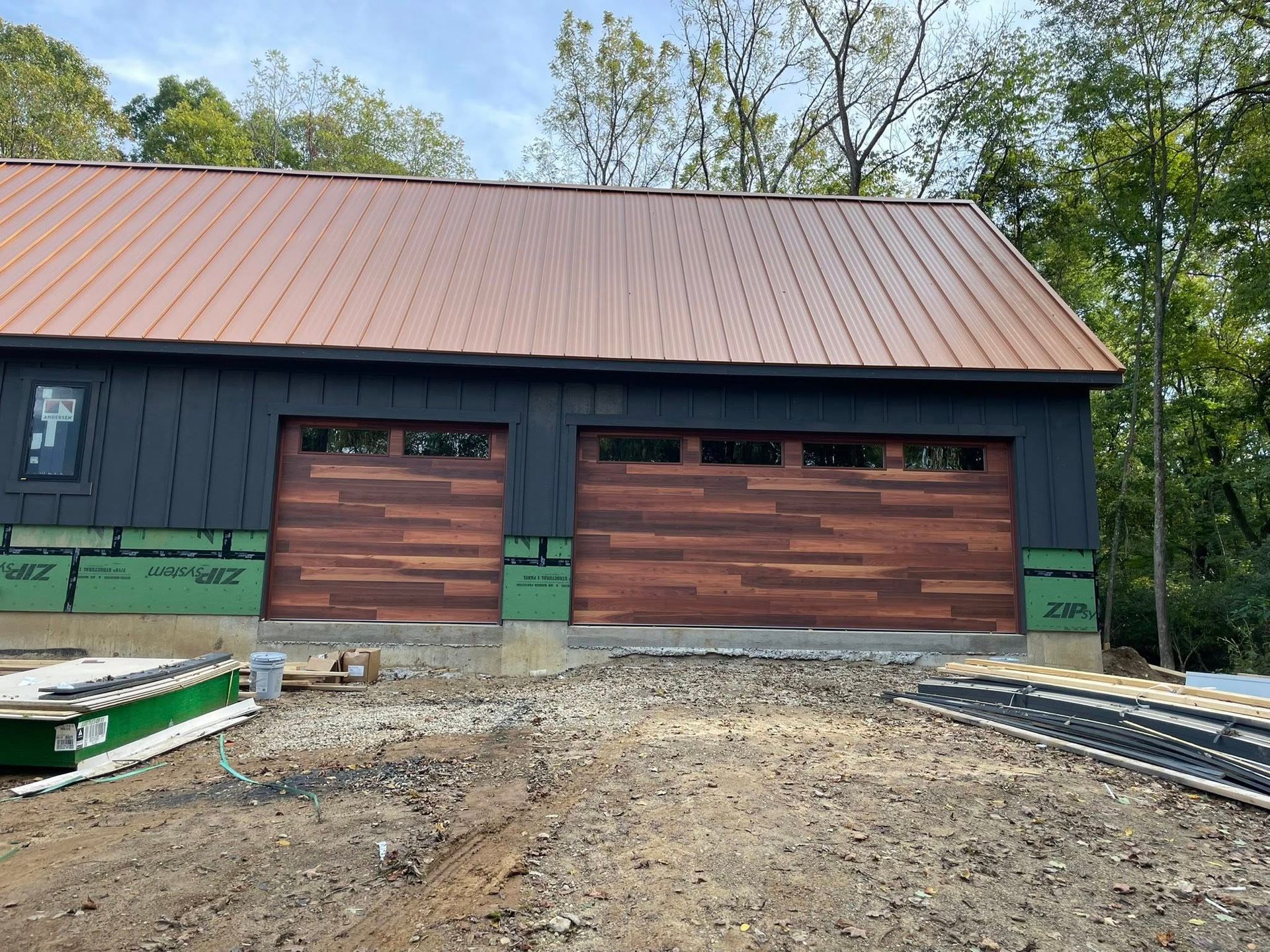 A new structure with a copper-colored metal roof and black siding, featuring two wood-paneled garage doors.