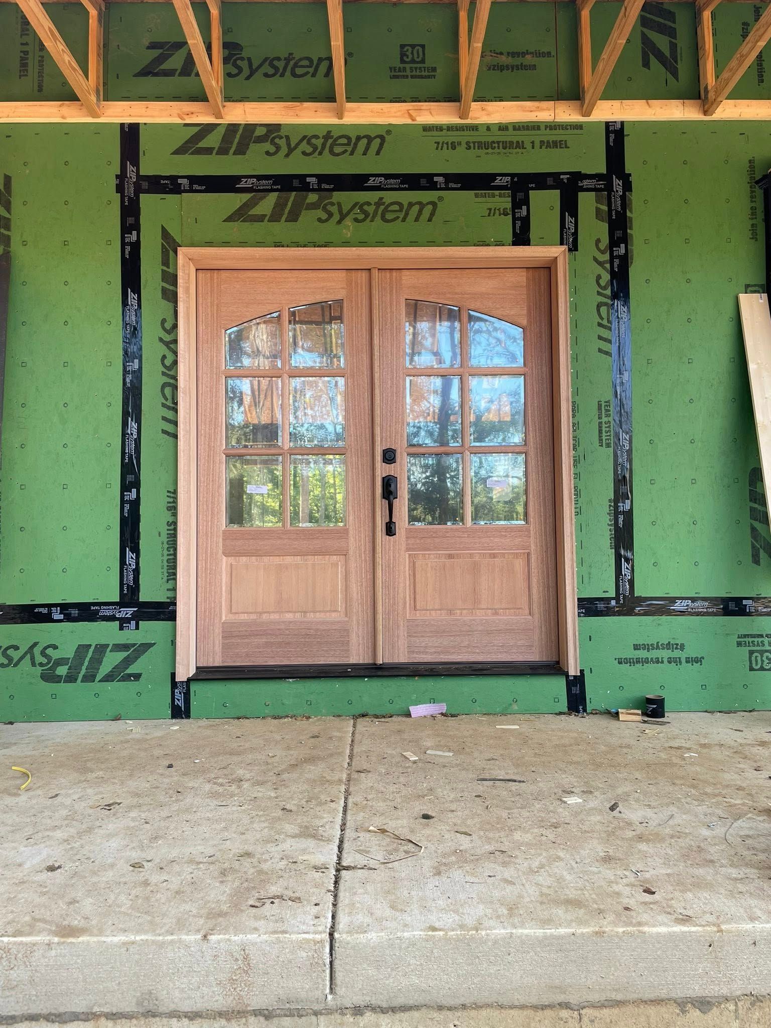 Double wooden French doors installed in an unfinished house exterior with green ZIP System sheathing.