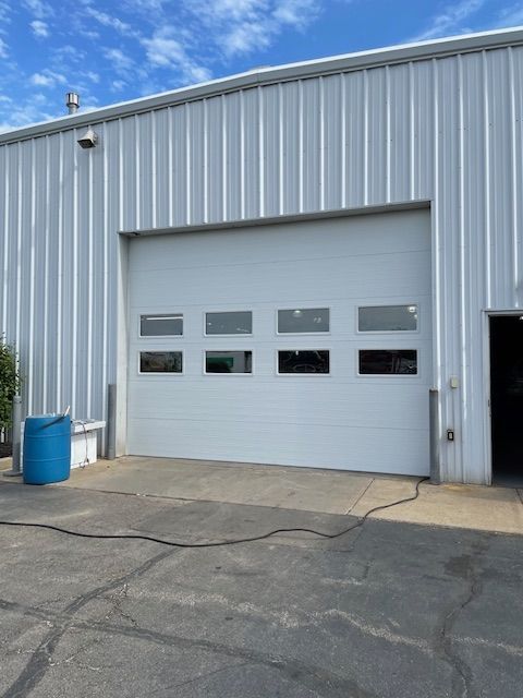 Exterior of a warehouse with a large, white overhead garage door featuring two rows of rectangular windows.