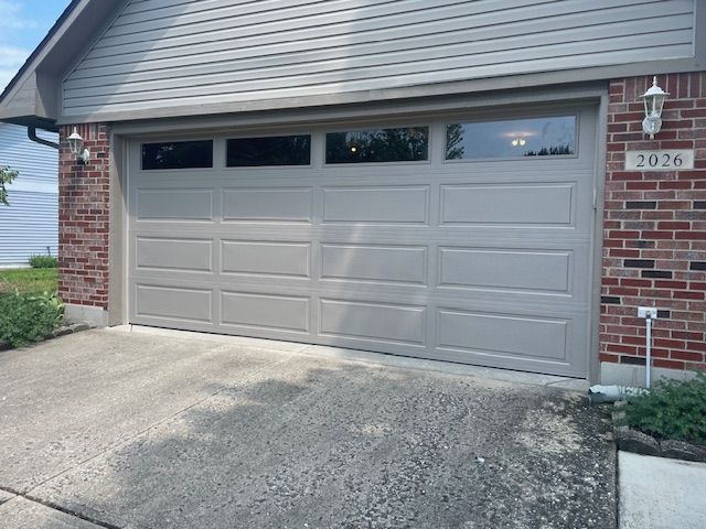 A neutral-colored garage door with four rectangular windows above, set into a red brick residential house exterior.