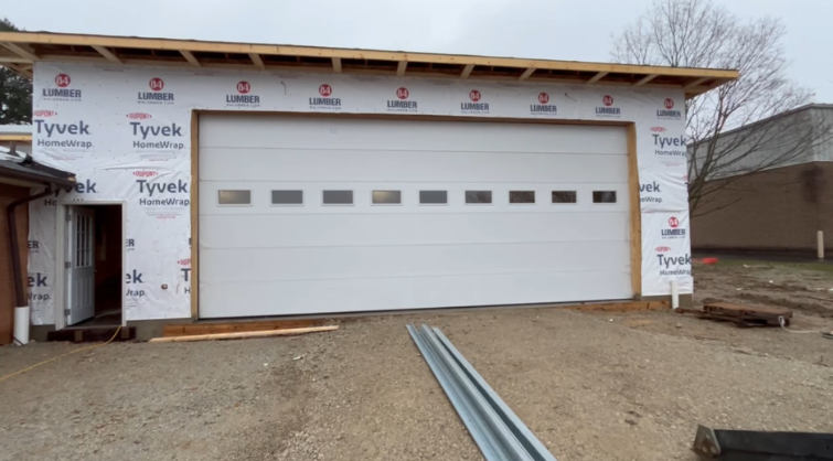 A newly constructed garage building with white siding, a door with windows, and Tyvek weather barrier wrap on the exterior.