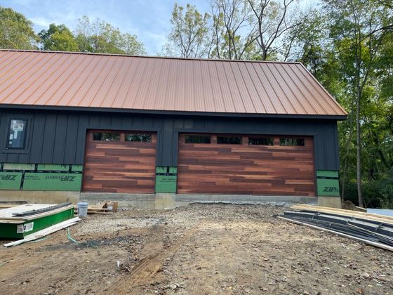 A garage under construction with a copper-colored metal roof, black vertical siding, and wood-finish garage doors.