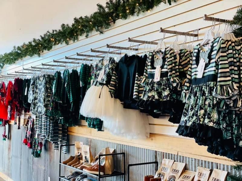 Racks of patterned clothing and dresses displayed along a boutique wall with shelves beneath